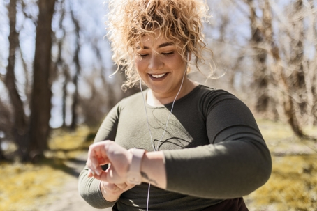 Woman smiling while checking her heart rate on an exercise watch while jogging.