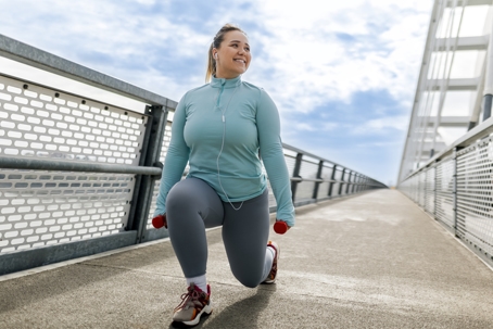Woman smiling while doing lunges on a bridge. She is happy to be taking control of her personal weight loss journey. | Soza Weight Loss