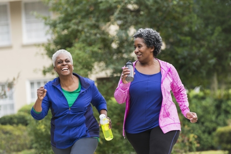 Two women taking a walk together in the spring. They are laughing and carrying water bottles.