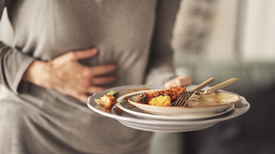 Person holding their stomach with discomfort after eating, illustrating acid reflux or digestive issues related to food intake.