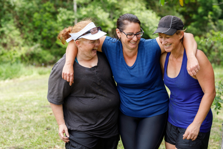 Three women smiling and walking together outdoors, showing support and encouragement in a shared weight loss journey.